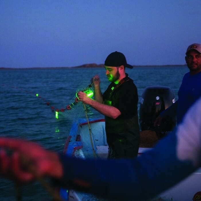 Jesse Senko at night, at sea, looking at a fishing net