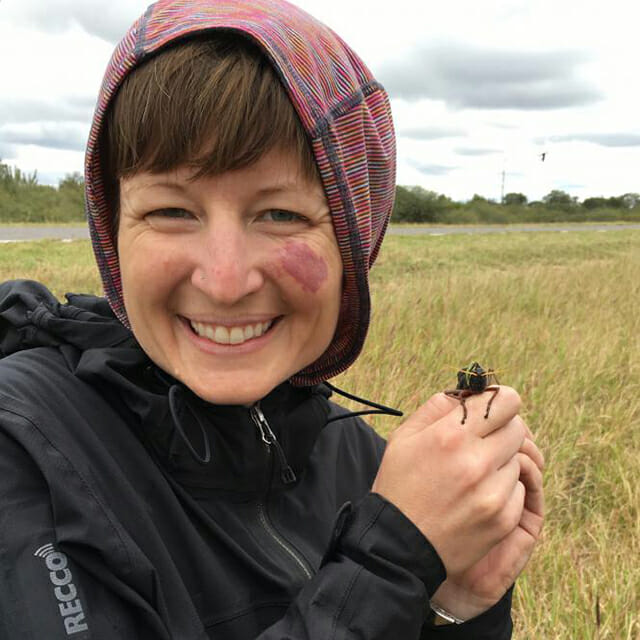 Arianne wearing a black jacket and smiling with a locust on her hand