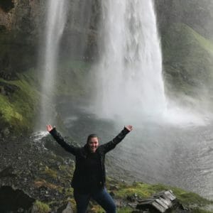 Woman with arms raised smiling in front of waterfall