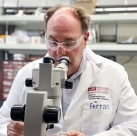 Man wearing lab coat looks into microscope
